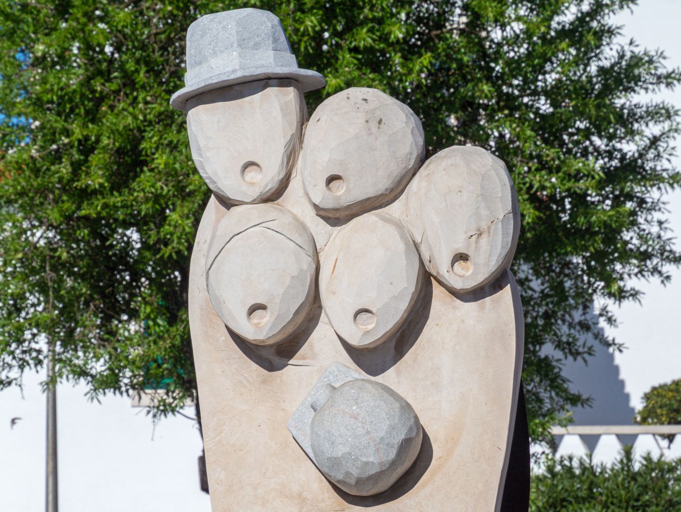 Photograph of a public art installation celebrating Cante Alentejano, showing five abstract carved heads with circular mouths singing. one wearing a hat