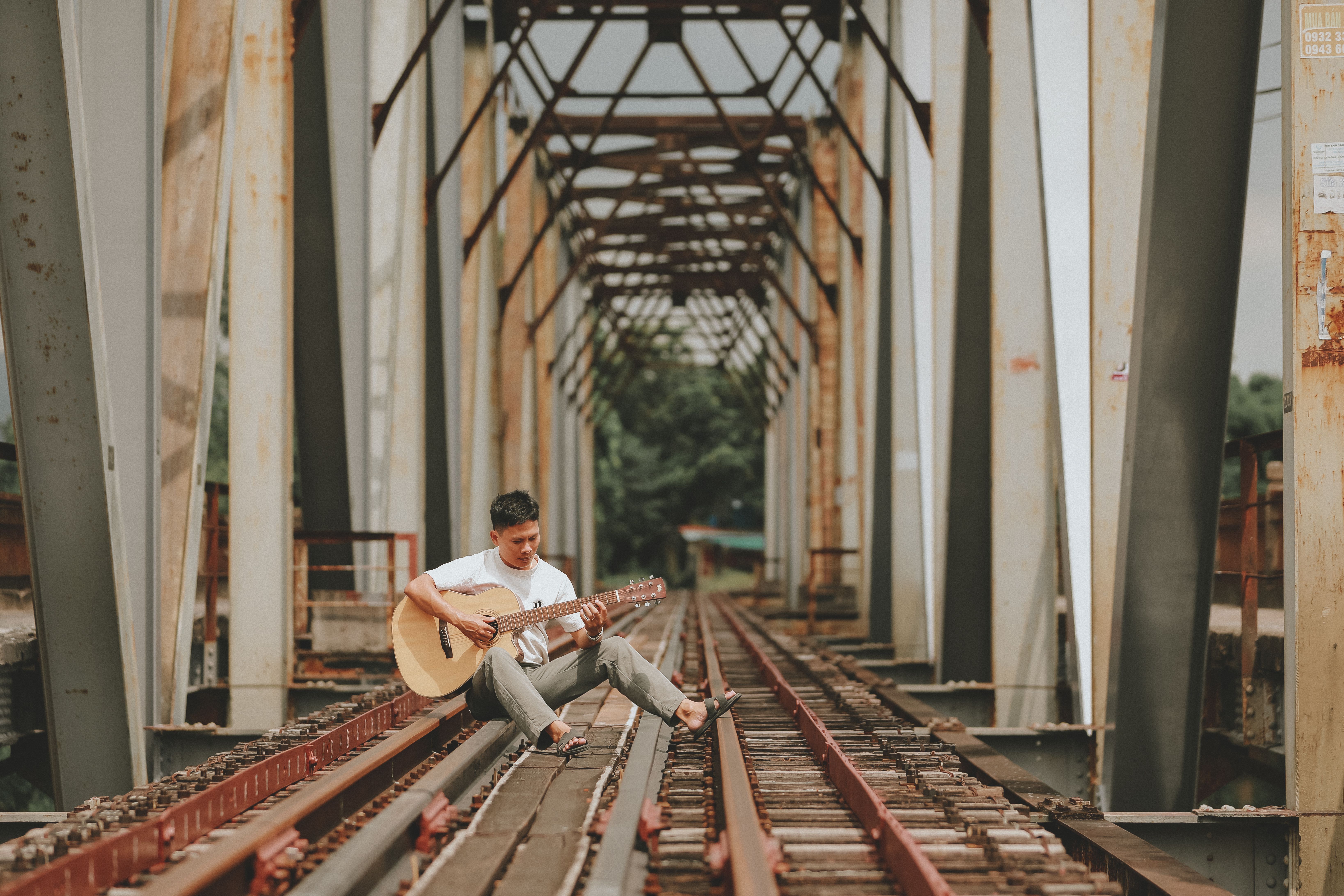 A man strumming a guitar on a rail bridge, perhaps playing his own train songs.